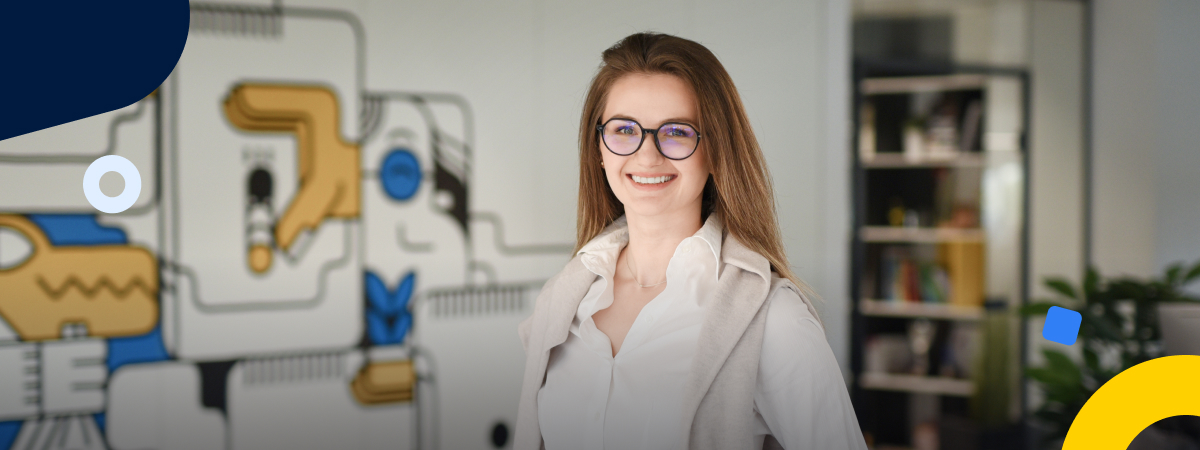 Monika Snitke wears glasses and smiles while standing in front of TransferGo branding