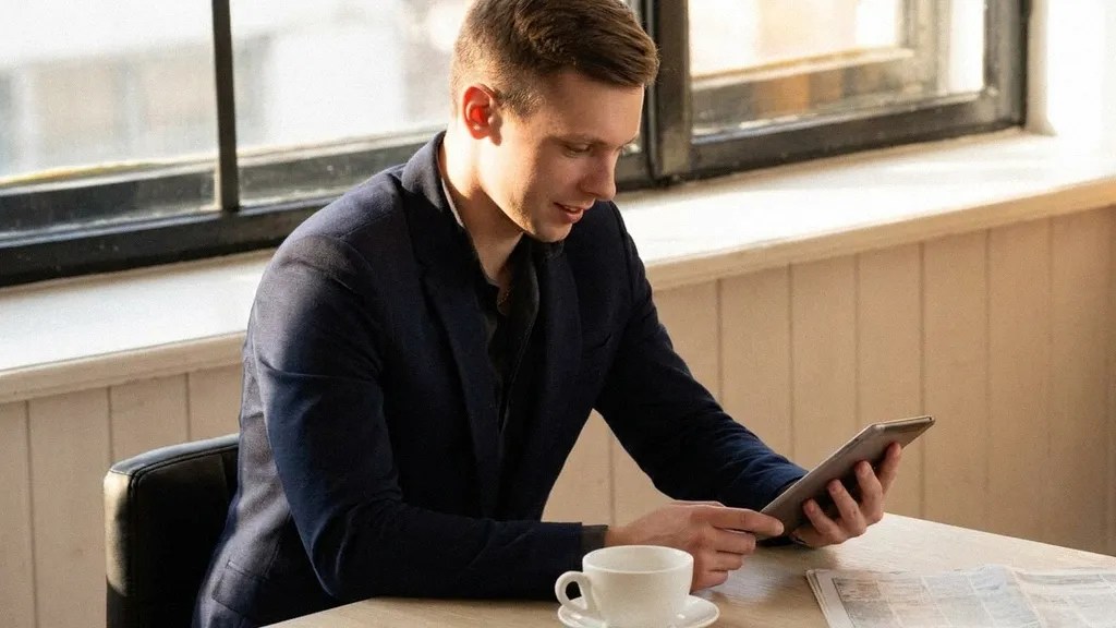 A young white male sits at his desk and reads an article on his tablet titled, 'Is Lloyds Business safe?'
