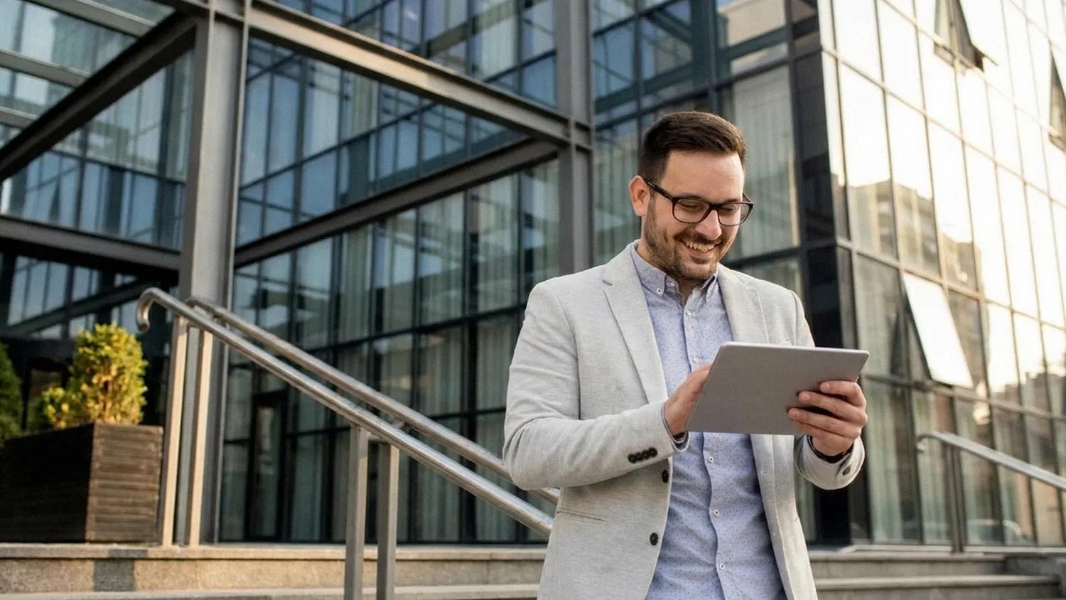 A young man in a casual shirt and suit stands outdoors and smiles as he holds his ipad and reads an article on 'Is Wise Business safe?'