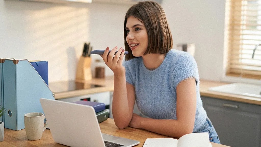 A young female with a short brunette bob sits at a table and talks to her smartphone on speakerphone as she commences the process to open bank account in Lithuania