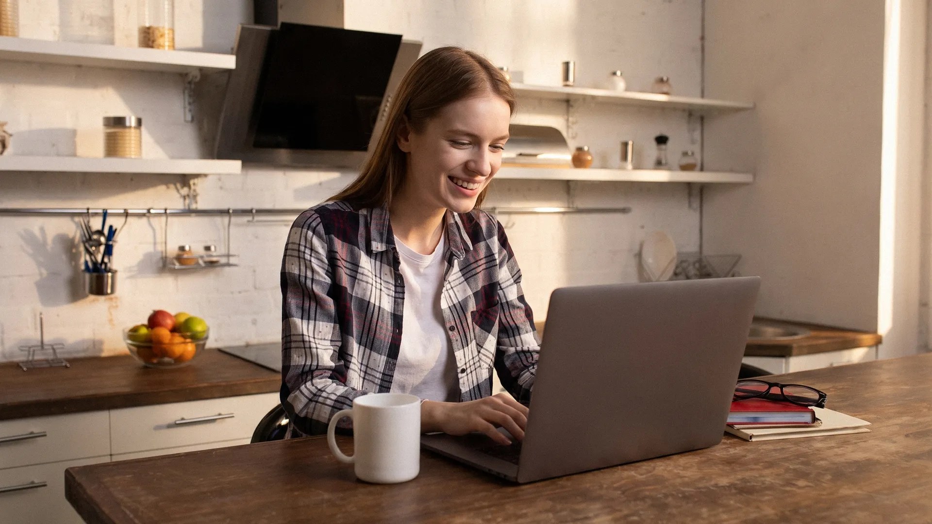 A young female sits at the table reading an article on her laptop about TransferGo vs PayPal Business